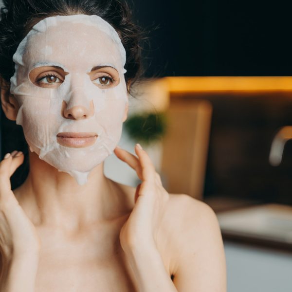 Female with naked shoulders uses rejuvenation facial sheet mask. Skin treatment at home, skincare