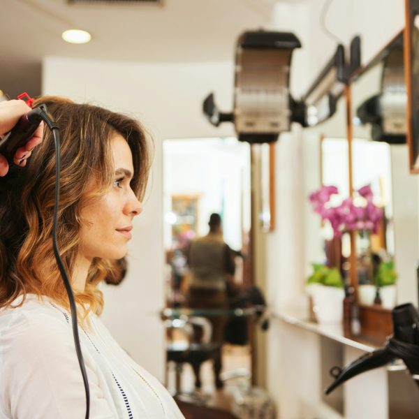 Hairdresser using curling tongs on customer's long brown hair in salon